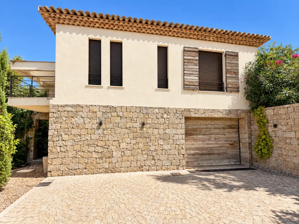 Porte de garage sectionnelle en bois et fenêtres BSO bronze pour villa à Saint-Tropez.