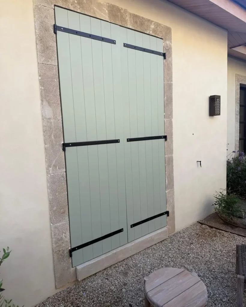 Volets battants en bois vert sauge sur encadrement en pierre à Saint-Tropez